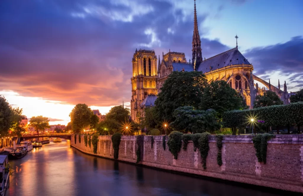Catedral de Notre-Dame de Paris iluminada ao pôr do sol, às margens do rio Sena, com arquitetura gótica e céu colorido ao fundo