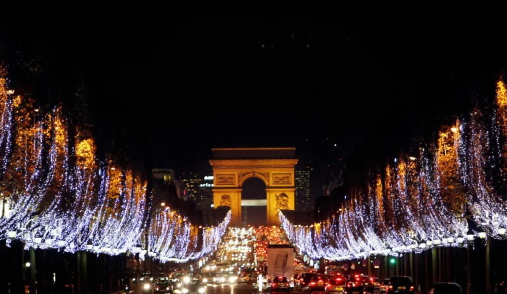 Avenida Champs-Élysées iluminada para o Natal à noite em Paris, com o Arco do Triunfo ao fundo e árvores cobertas por luzes.