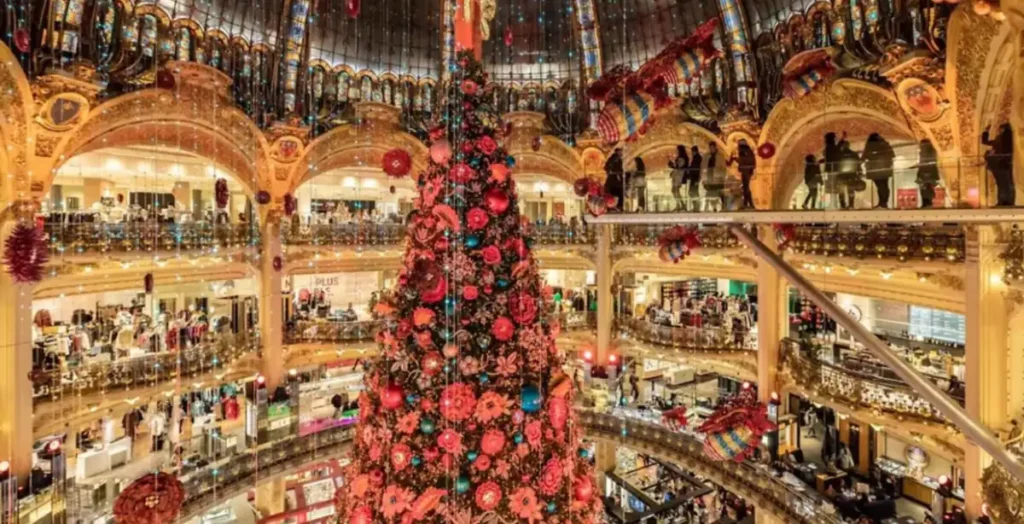 Árvore de Natal gigante no interior da Galeries Lafayette em Paris, cercada pela arquitetura histórica e decoração natalina da loja.