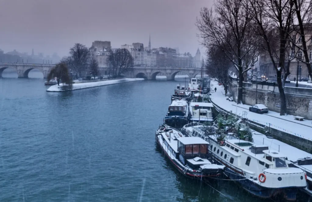 Paris no inverno: neve às margens do Rio Sena, com barcos e pontes compondo uma das paisagens mais charmosas da cidade.