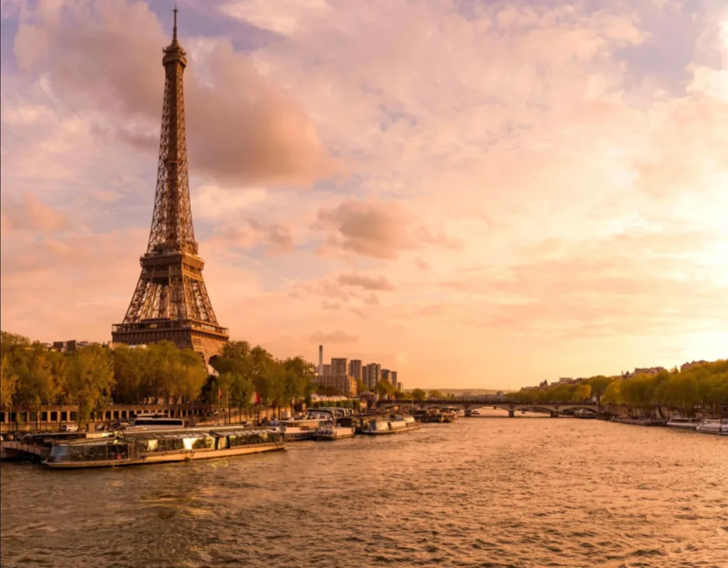Pôr do sol sobre a Torre Eiffel e o Rio Sena, com os tradicionais barcos de passeio de Paris.