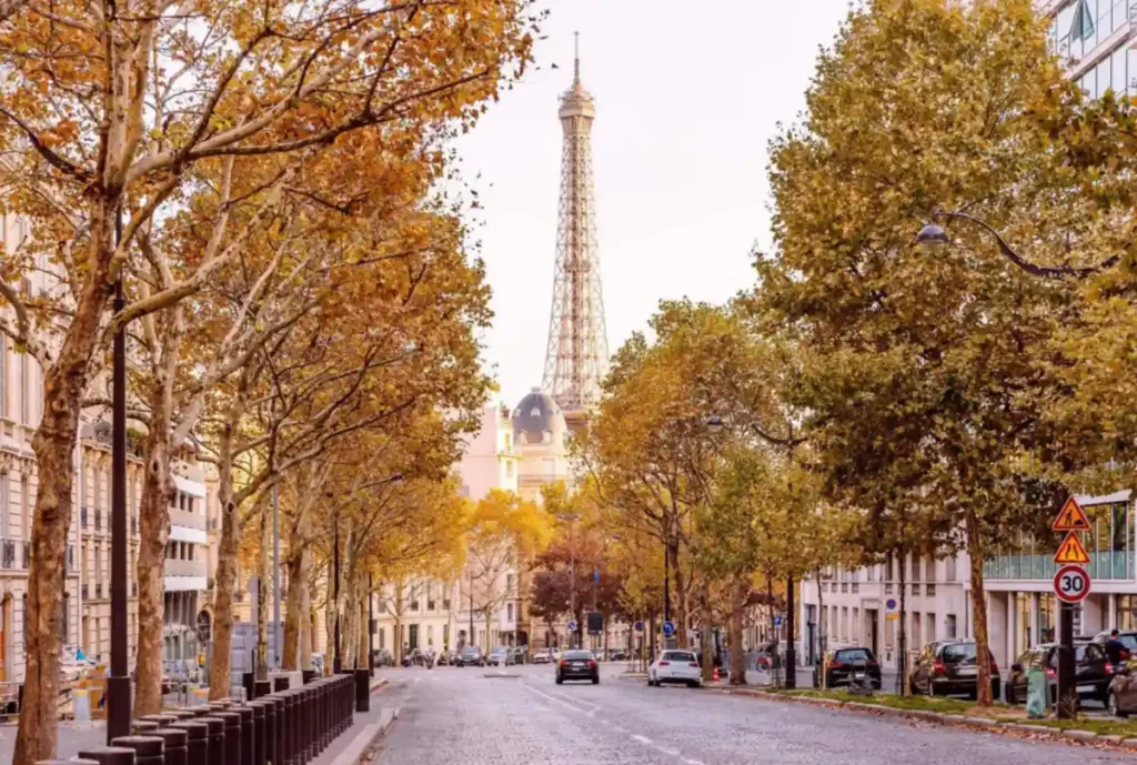 A Torre Eiffel surge entre edifícios e árvores douradas em uma charmosa rua de Paris durante o outono.