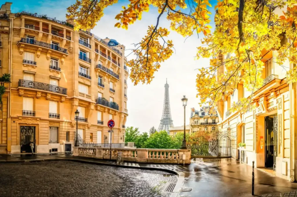 Uma vista da Torre Eiffel entre a arquitetura elegante e as árvores de outono de um bairro parisiense.